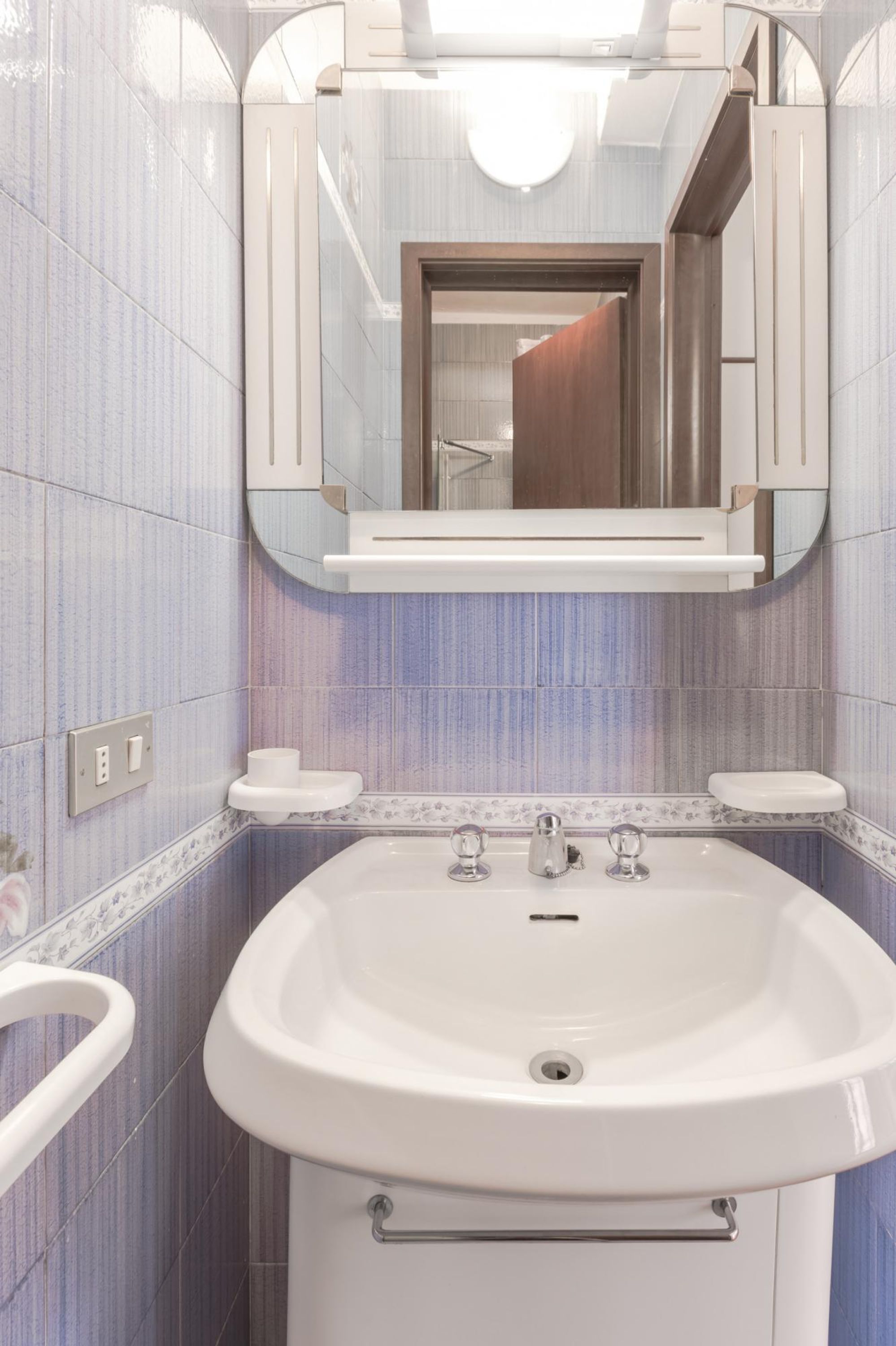 A bathroom with a white sink, two mirrors, and a toilet.