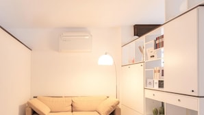 A modern living room with a beige sofa, a white air conditioner, and a bookshelf with books and decorative items. - Casa Saronni by Wonderful Italy (Bellagio)
