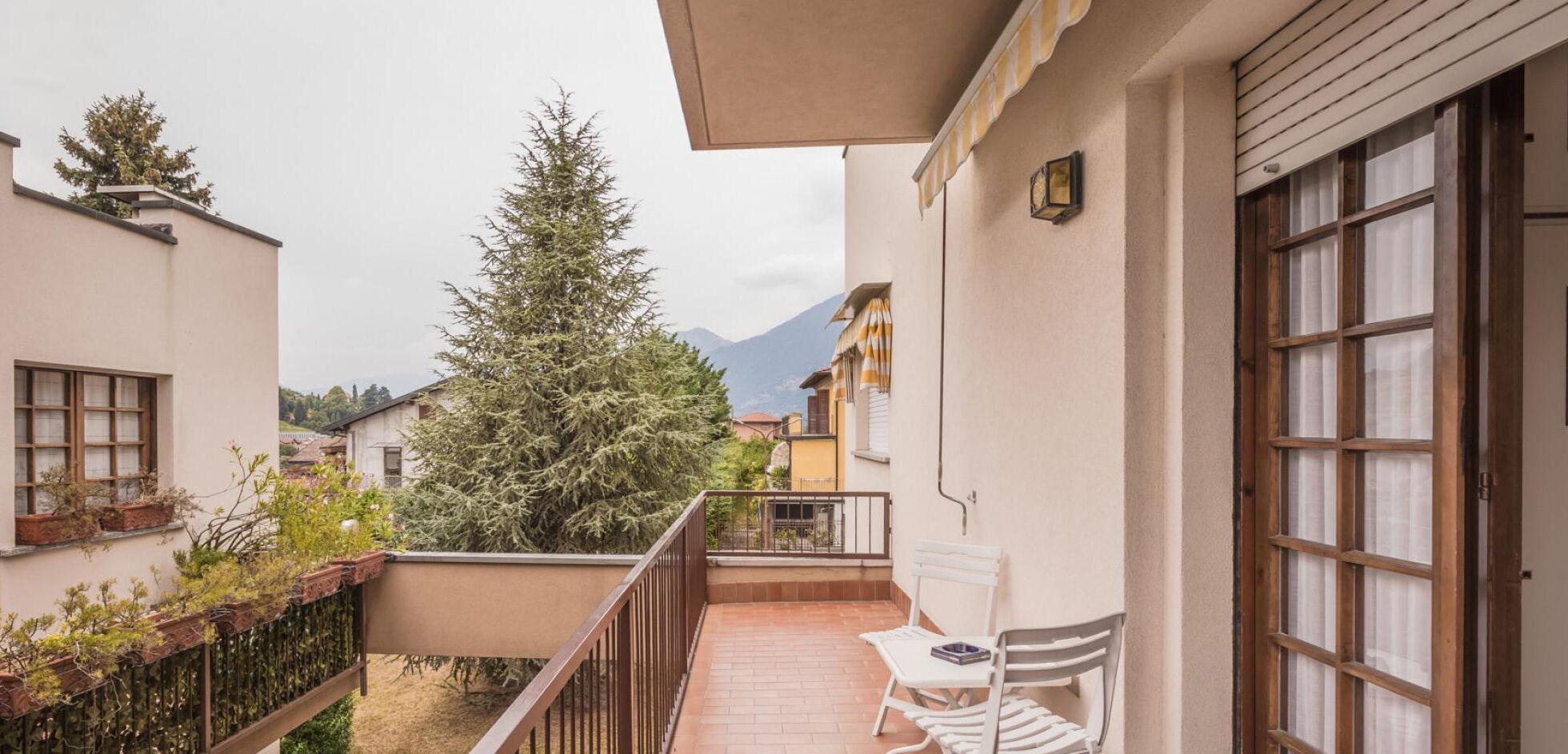A balcony with a view of a mountain, a large evergreen tree, and a white chair.