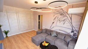 Ein modernes Wohnzimmer mit einem grauen Ecksofa, einem schwarzen Couchtisch mit Obst, einem schwarzen Sessel und einer Wand-Klimaanlage.