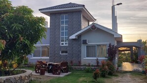 A modern house with a stone facade, a large window, and a patio with a table and chairs. - Casa Atalaya - 2 BR seaview Home at Calatagan (CALATAGAN)