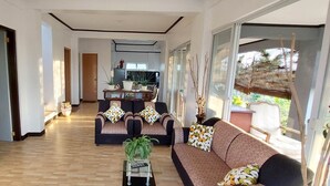 A spacious living area with a sofa set, a coffee table, and a TV. There is a dining area in the background with a table and chairs. - Casa Atalaya - 2 BR seaview Home at Calatagan (CALATAGAN)