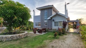 A modern house with a stone facade, a patio with a table and chairs, and a garden with various plants. - Casa Atalaya - 2 BR seaview Home at Calatagan (CALATAGAN)