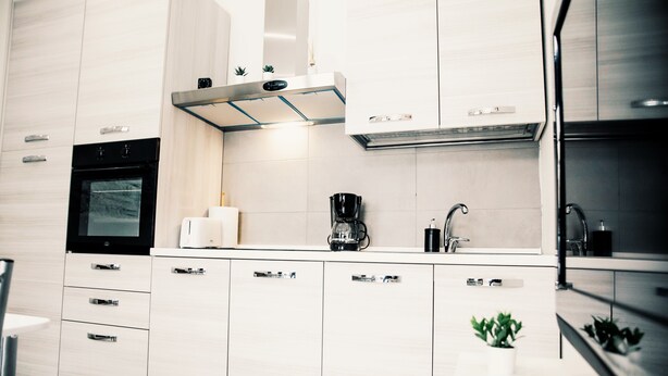 Une cuisine moderne avec des meubles blancs, un four encastré, une machine à café et un évier.