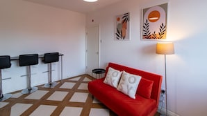 A modern living room with a red sofa, three black bar stools, a floor lamp, and two abstract wall art pieces. - Beautiful 1-bed Apartment in Gateshead (Gateshead)