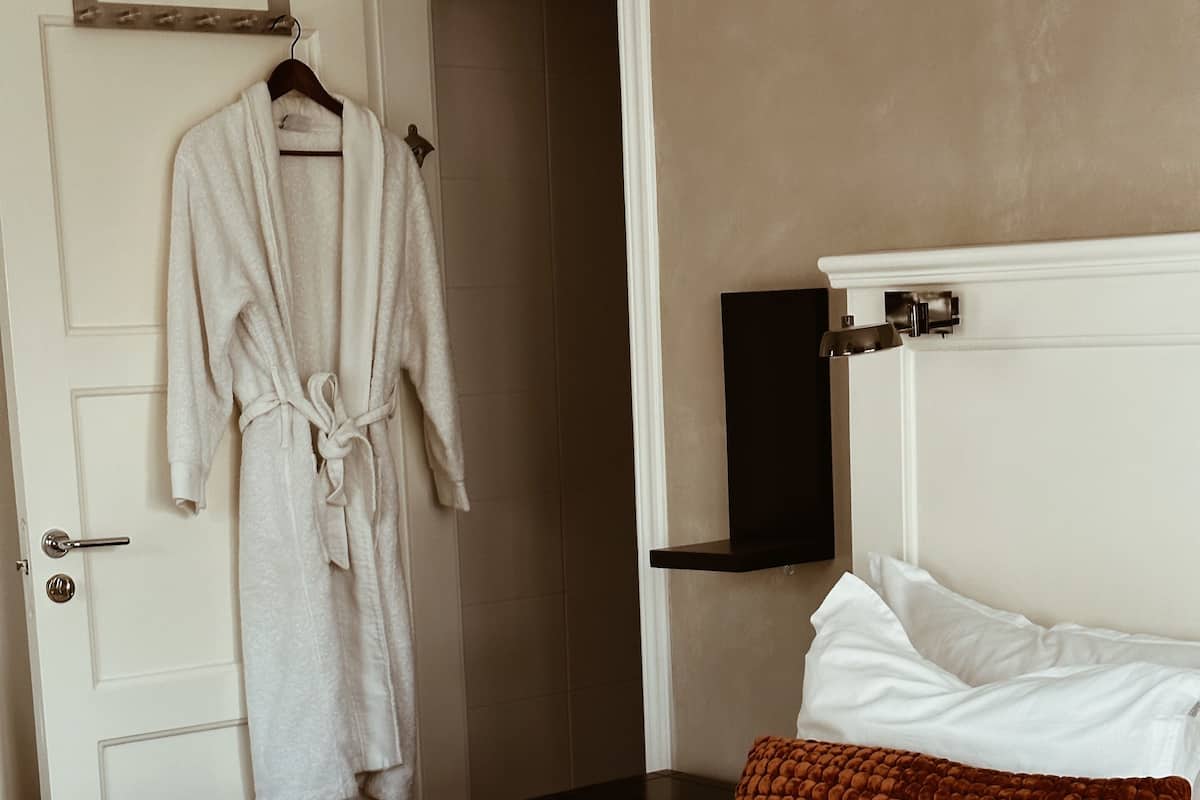 A hotel room with a bed, a robe hanging on the door, a television on the wall, and a brown pillow.
