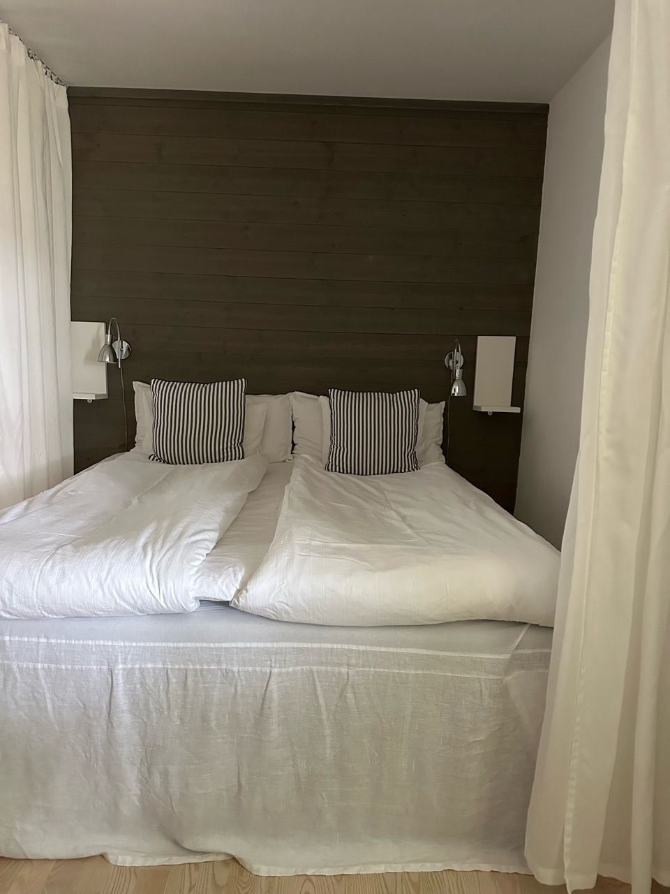 A bed with a dark headboard, white bedding, and two bedside lamps.