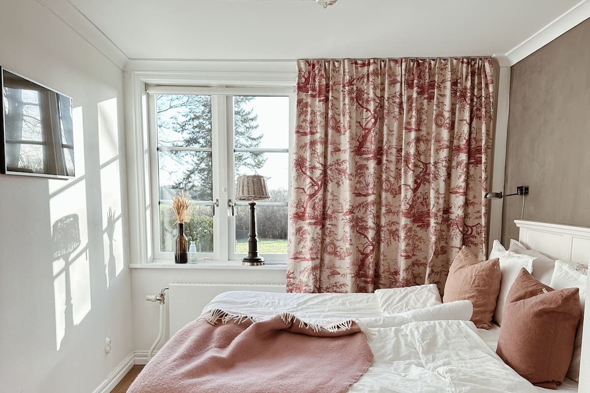 A bedroom with a bed, a window, a radiator, and a lamp.