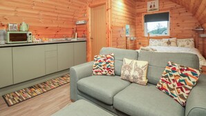 Un acogedor interior de cabaña con kitchenette, un sofá con cojines estampados y una ventana con vistas al exterior.