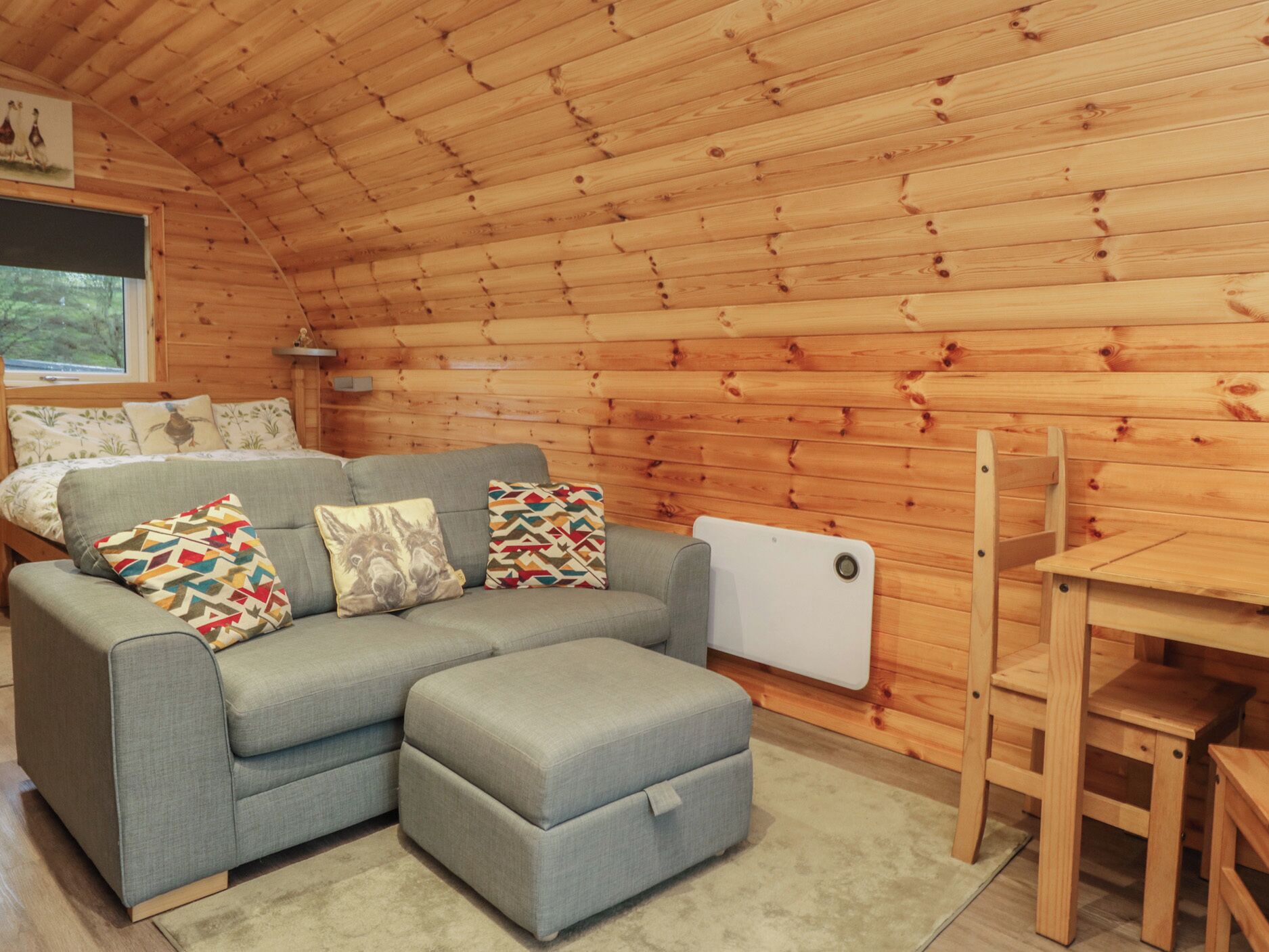 Un intérieur de chalet chaleureux avec un canapé gris, un pouf, des murs en bois et une fenêtre.