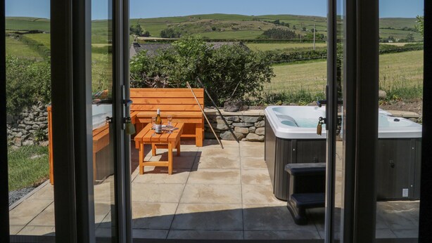 Un patio con mesa y sillas de madera, un jacuzzi y un muro de piedra.