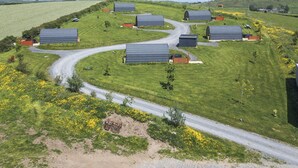 Paisaje rural con varias construcciones pequeñas, un camino serpenteante y un campo de flores amarillas.