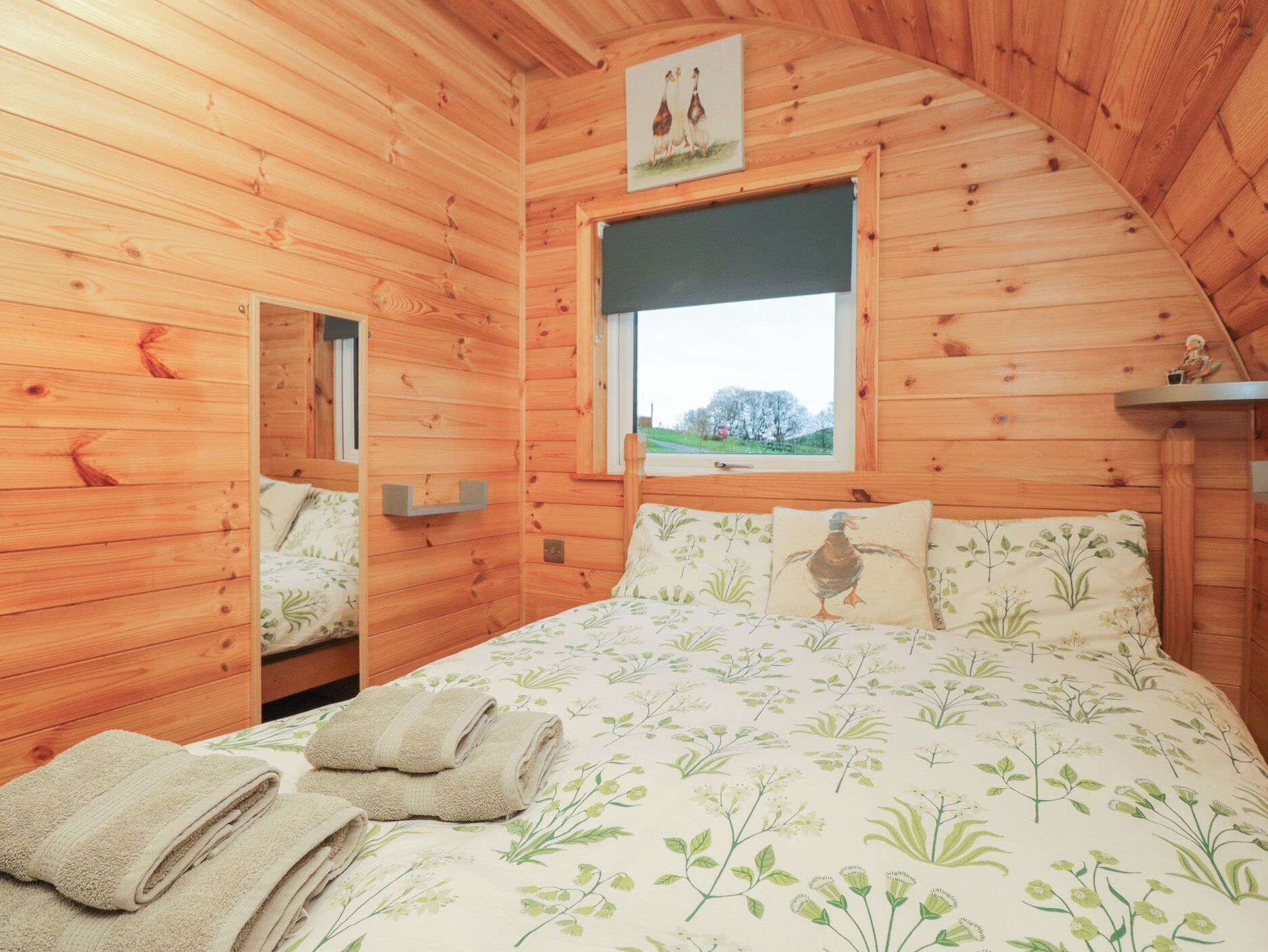 Une chambre dans une cabane en bois, avec un lit, des oreillers et une fenêtre donnant sur la campagne.