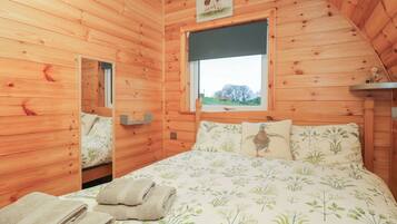 Une chambre dans une cabane en bois, avec un lit, des oreillers et une fenêtre donnant sur la campagne.