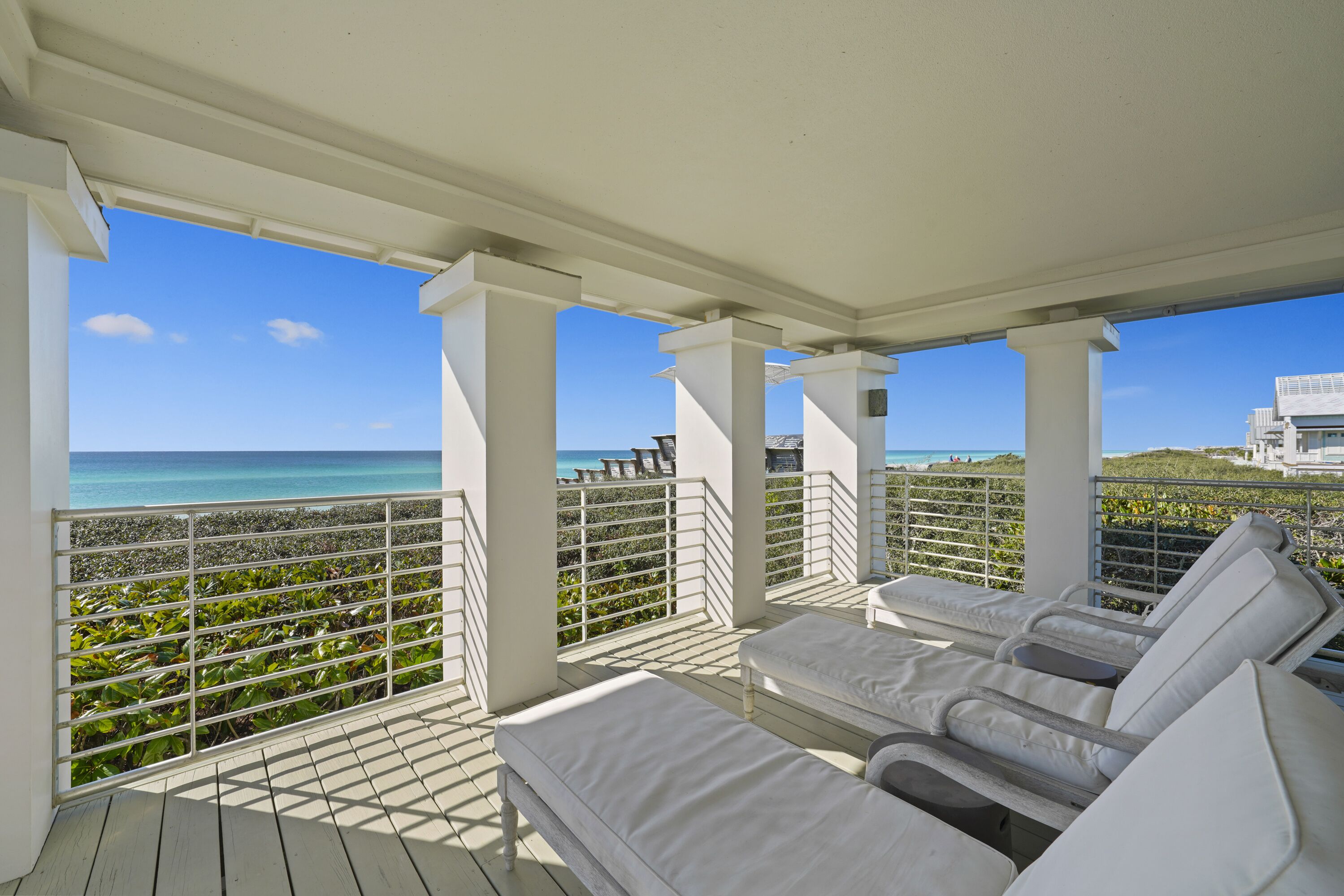A covered outdoor seating area with white cushioned chairs and a view of the ocean.