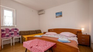 Une chambre à coucher avec un lit en bois, une table de chevet, une chaise, une petite table et une fenêtre avec un rideau.