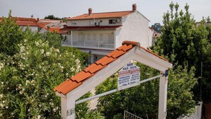Une enseigne indiquant une maison nommée « DOM HAUS », avec un toit rouge, entourée de verdure.