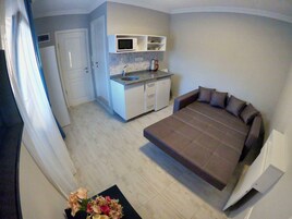 A compact bedroom with a bed, a small kitchenette, and a door leading to another room.