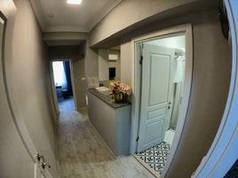 A hallway with a tiled floor, a door leading to a bathroom, and a small counter with a vase of flowers.