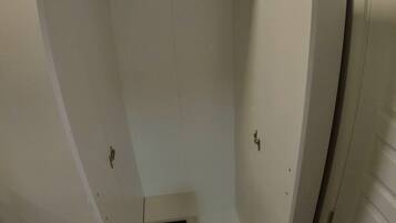 Een kamer met douche, een deur en een kleine ventilatieunit aan de muur.