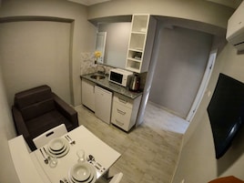A compact kitchen with a microwave, sink, and white cabinets. There is a dining area with a table set for two.