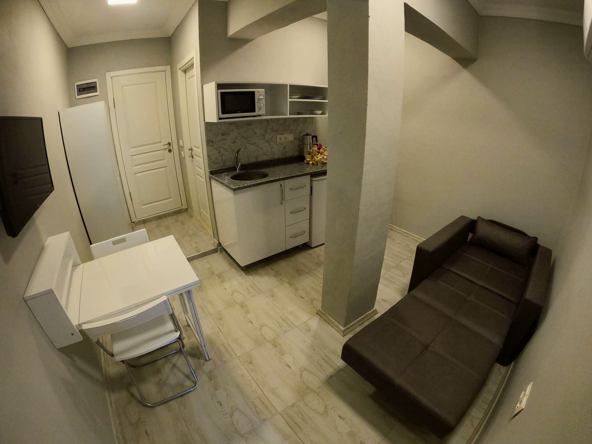 A compact living space with a kitchenette, a small dining table, a sofa, and a white cabinet.