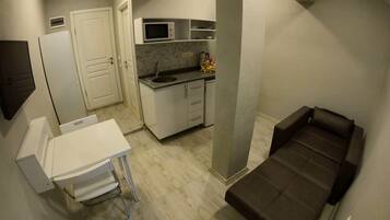 A compact living space with a kitchenette, a small dining table, a sofa, and a white cabinet.