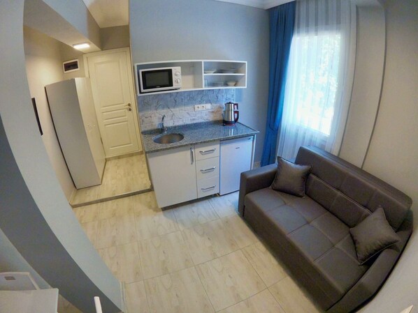 A compact living space with a kitchenette, a sofa, and a window with curtains. - Miralya Homes (Fethiye)