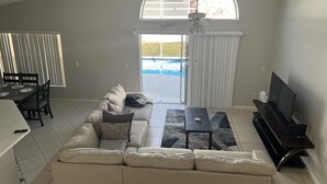 A spacious living room with a large sectional sofa, a TV, and a dining area with a table and chairs. - Beautiful house just 12min from Disney World! (Kissimmee)
