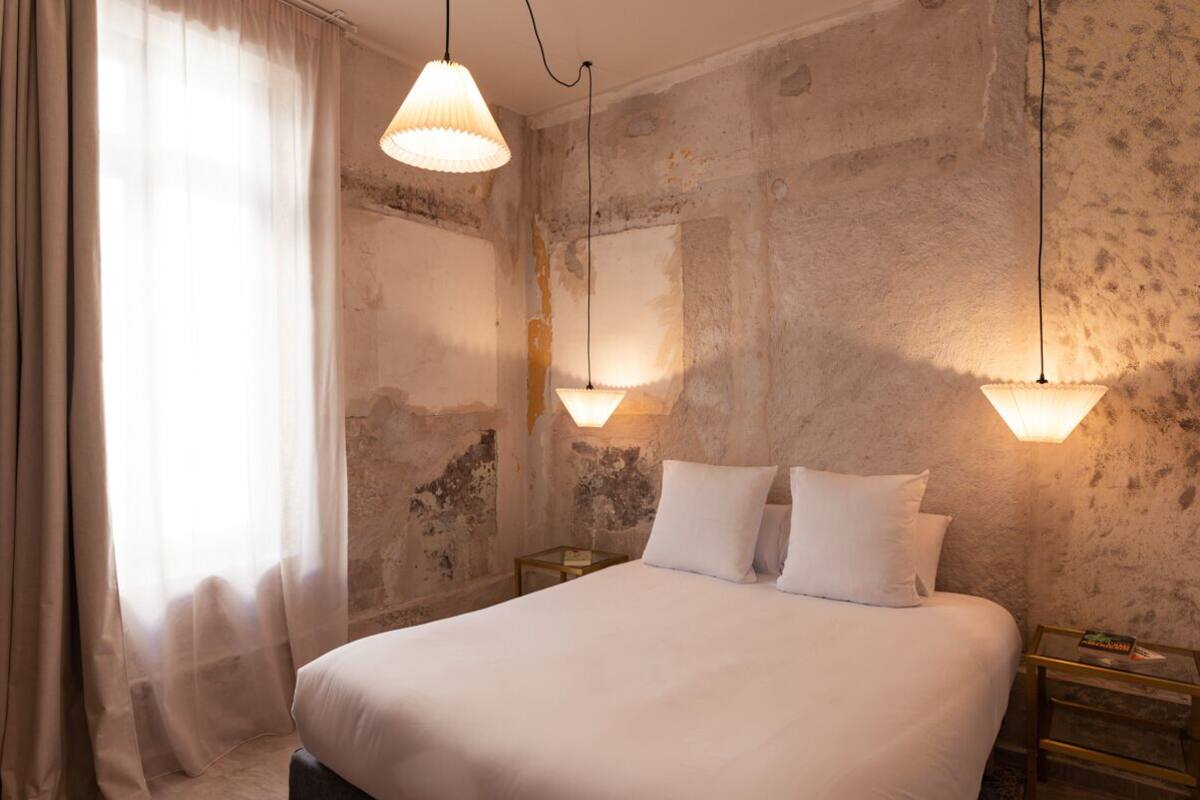 A room with a large bed, two bedside tables, and a window with sheer curtains.