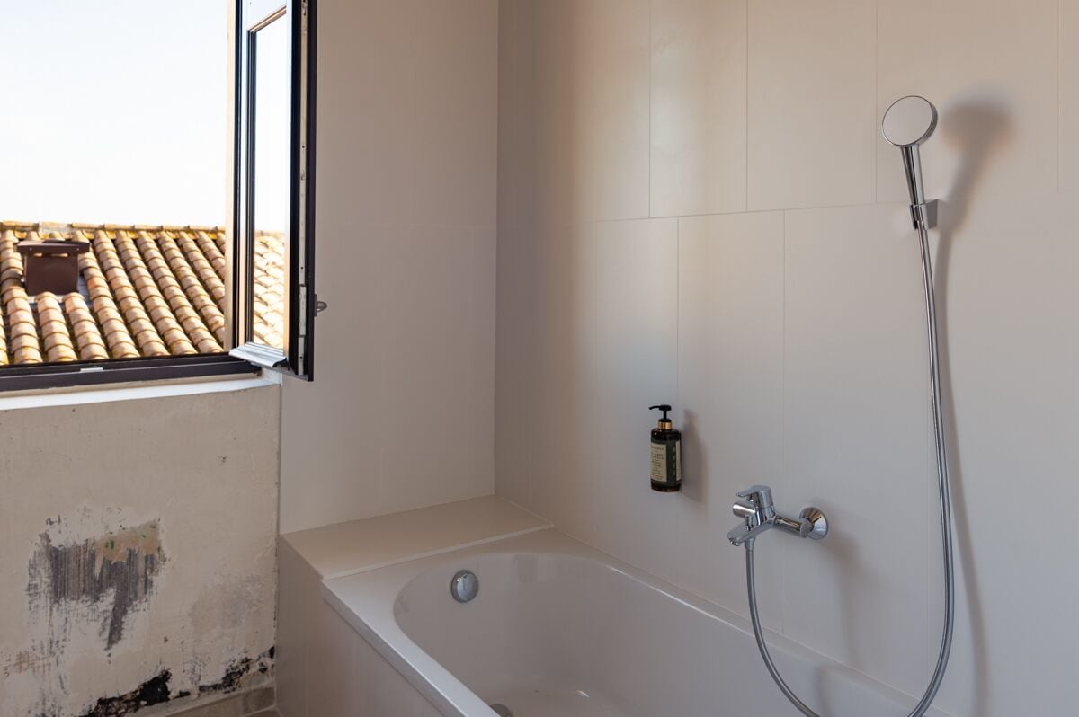 Een badkamer met een badkuip, een douche en een raam met uitzicht op een pannendak.