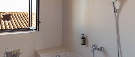 A bathroom with a bathtub, a shower, and a window overlooking a tiled roof.
