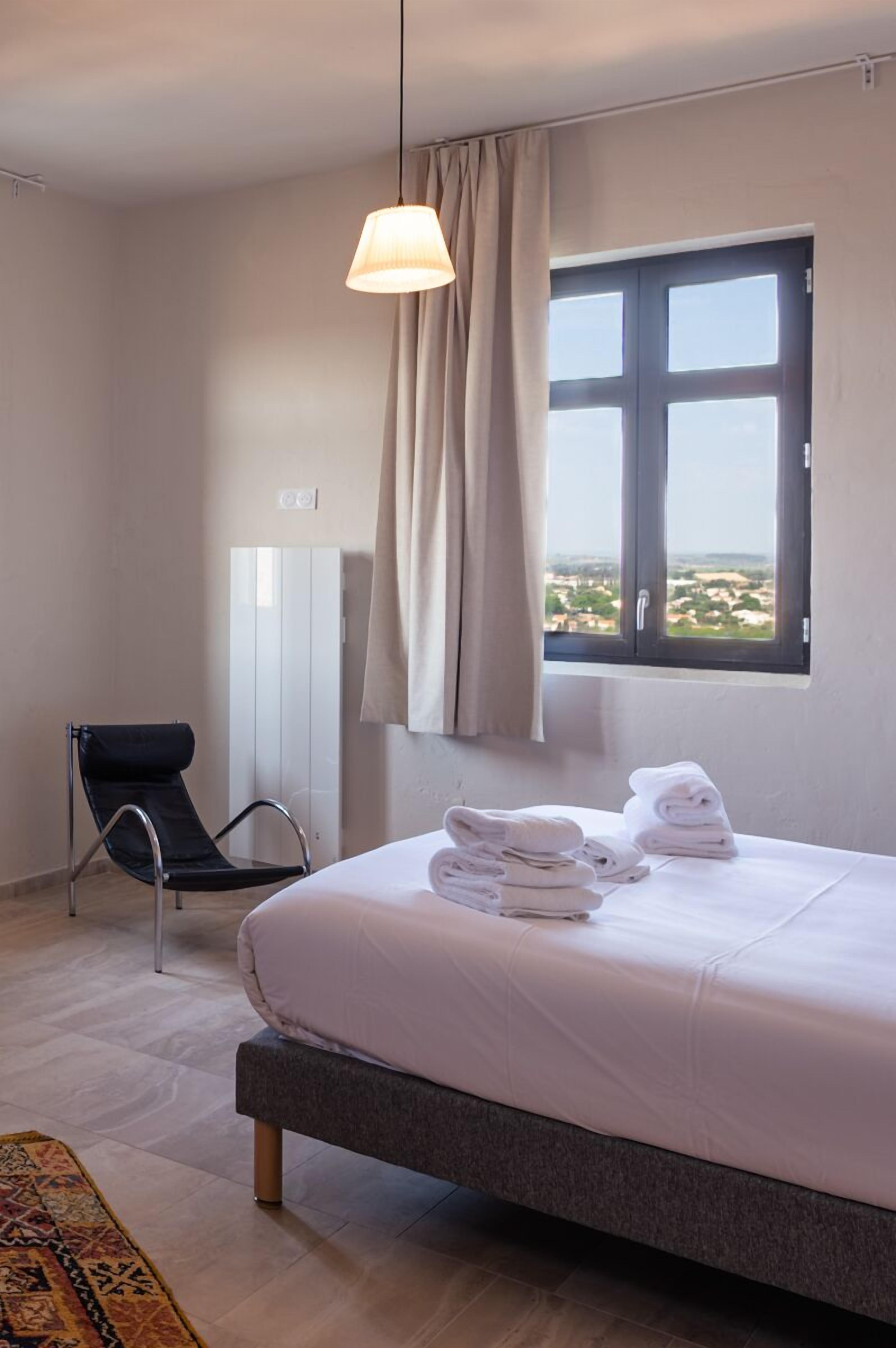 A hotel room with a bed, a chair, a window with curtains, and a view of the landscape.