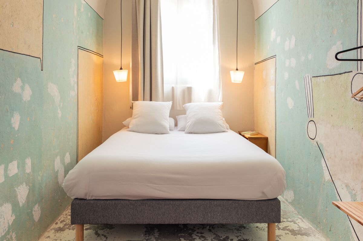 Una habitación estrecha y bien iluminada con una cama individual, dos mesitas de noche y un ventanal con cortinas.