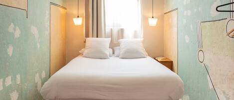 A narrow, well-lit room with a single bed, two bedside tables, and a large window with curtains.