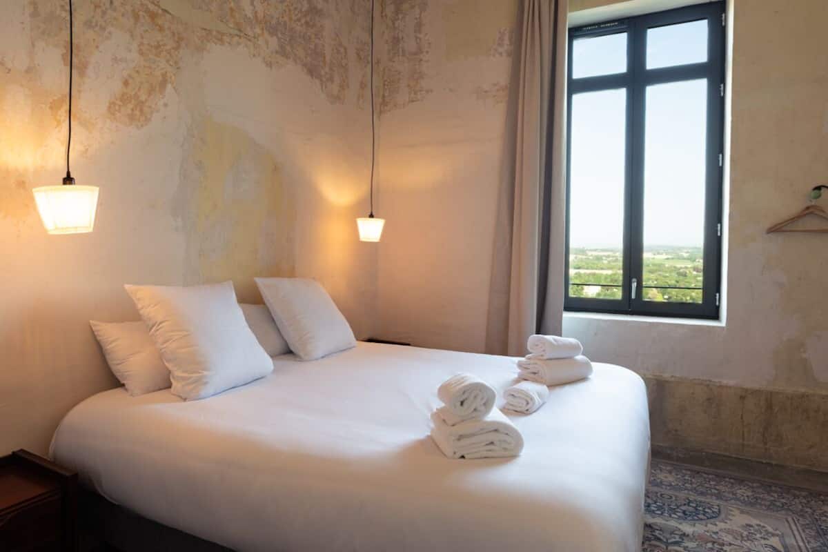 A hotel room with a large bed, two bedside lamps, a window with a view, and neatly folded towels on the bed.