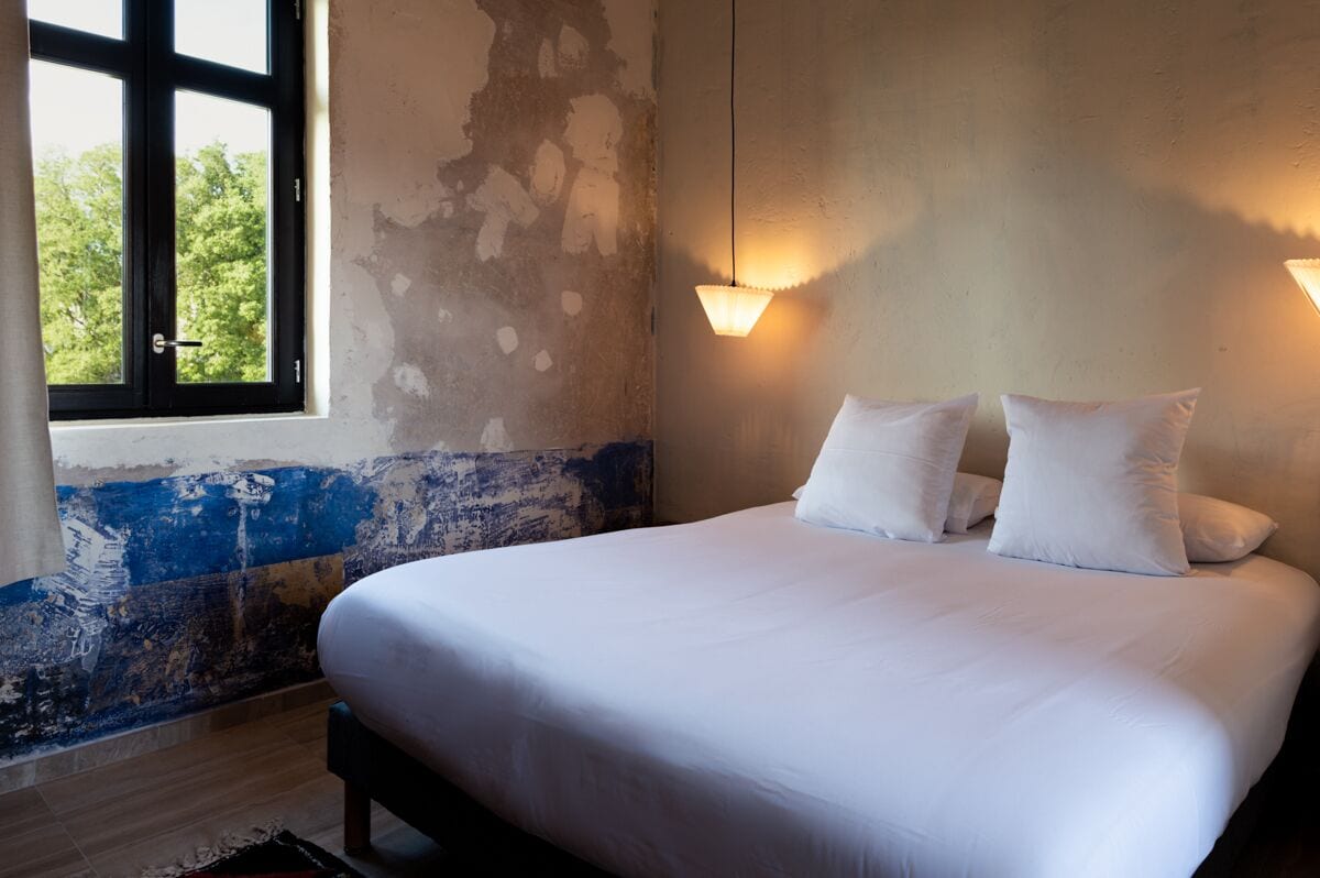 Un dormitorio con una cama grande, dos lámparas de pared, una ventana con vistas a árboles y una pared pintada a medias.