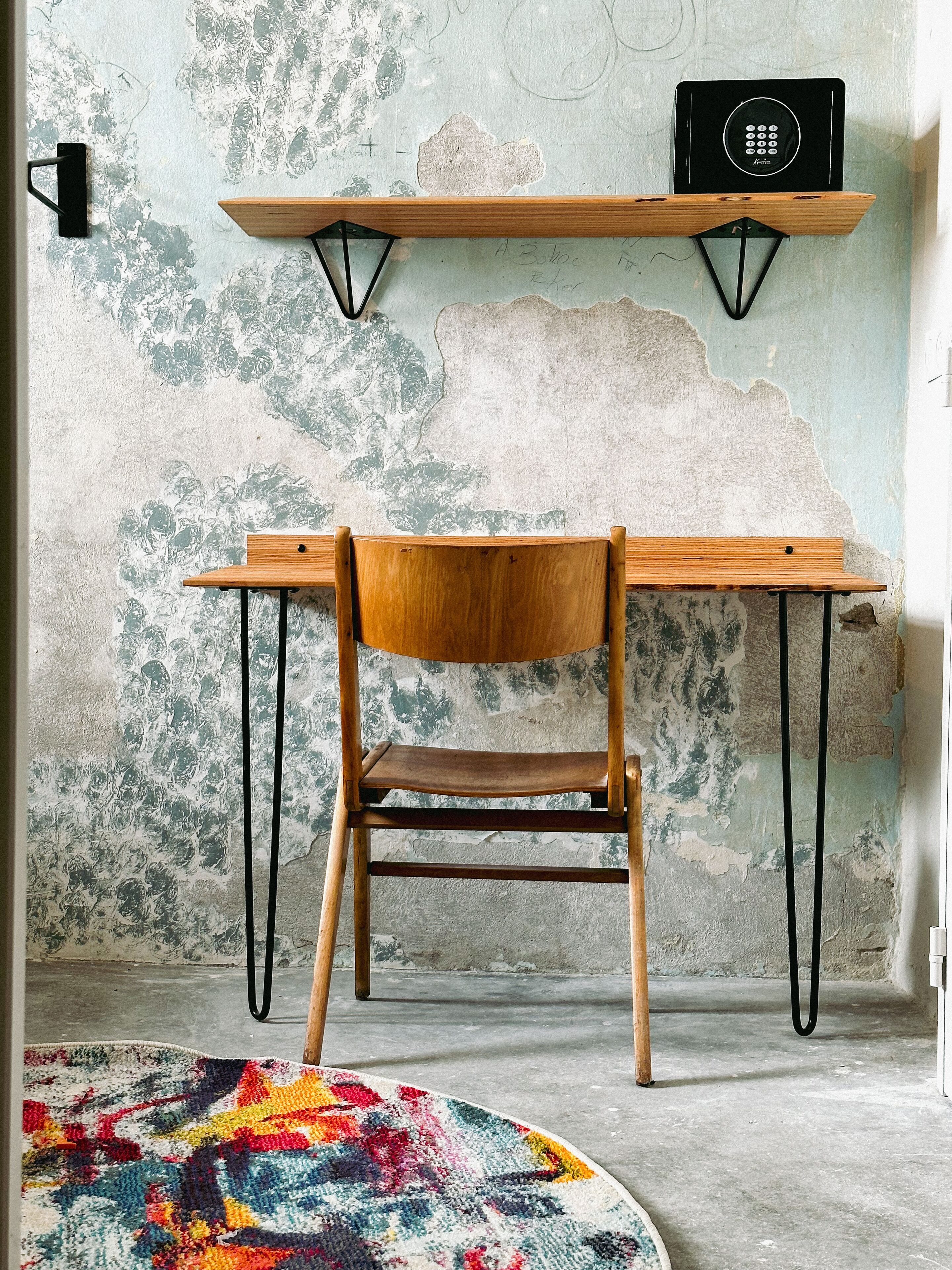Un bureau en bois avec une chaise, un tapis coloré et une étagère murale sur laquelle se trouve une radio.