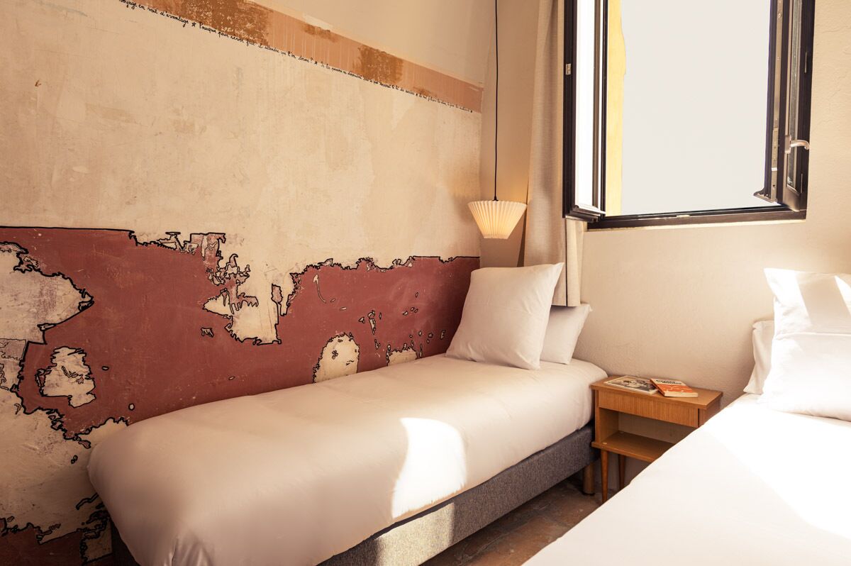 A hotel room with a large bed, a nightstand with a lamp, and a wall with a map design.