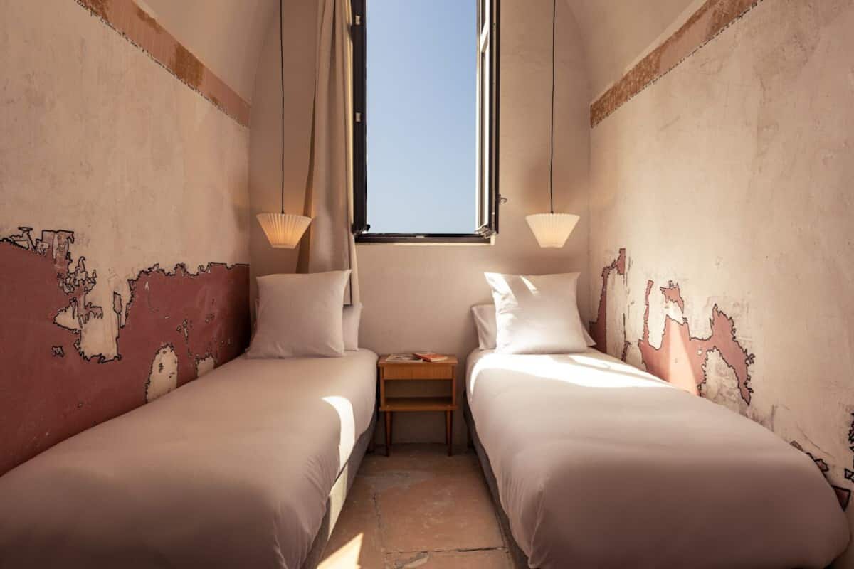 A small, cozy room with two beds, a nightstand, and a window.