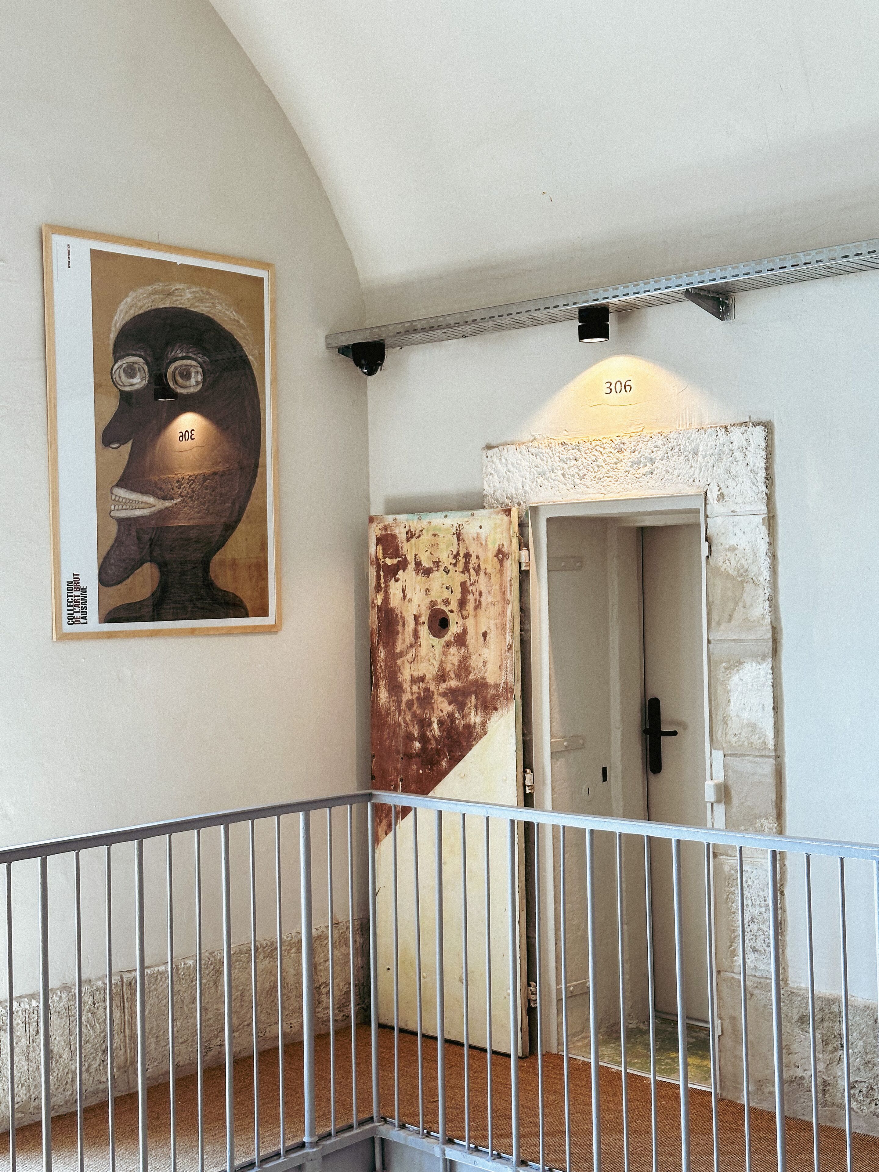 A corridor with a metal railing, a door with a number '306' above it, and a wall-mounted artwork.