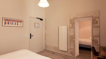 A bedroom with a bed, a desk, and a chair. There is a door with a calendar on it, and a wall with a stone accent.