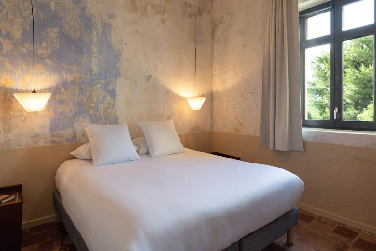 A bed with white linens in a room with textured walls and two wall-mounted lights.