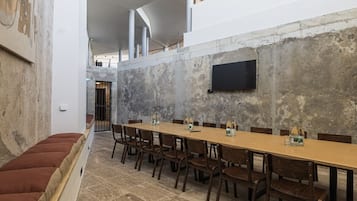 Une salle de conférence avec une longue table, des chaises en bois et un téléviseur à écran plat fixé au mur.