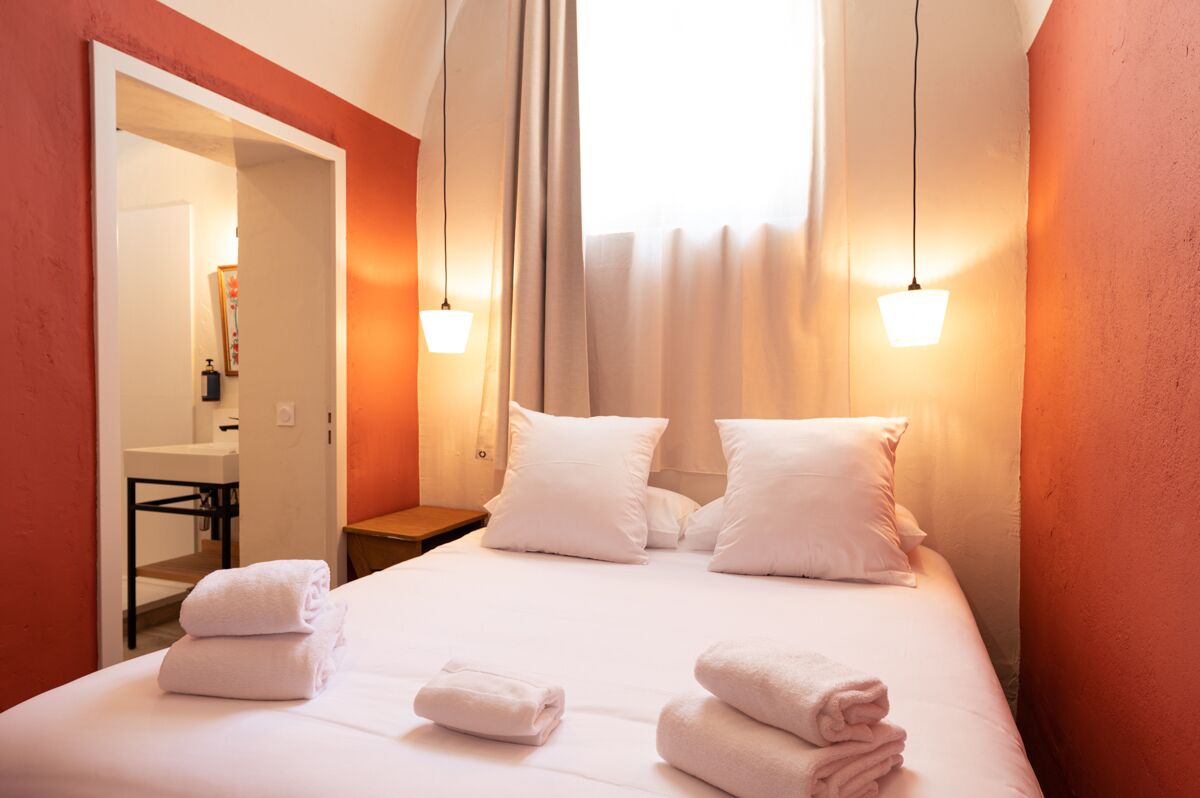 Habitación de hotel con cama, toallas blancas, mesita de noche, espejo y ventana con cortinas.