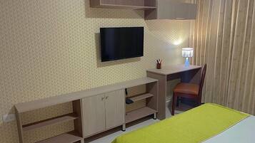 Hotellihuone, jossa on sänky, työpöytä tuolilla, televisio ja lamppu.