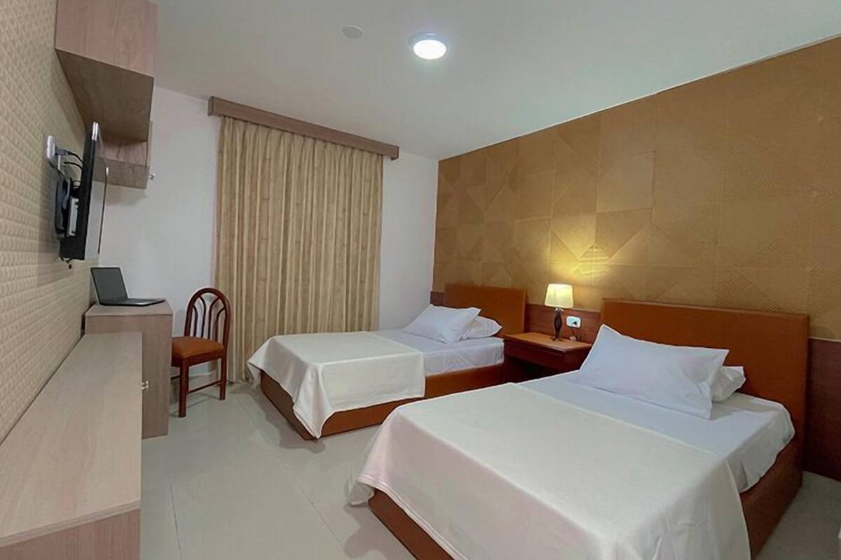 A hotel room with two beds, a desk with a laptop, a chair, and a TV mounted on the wall.
