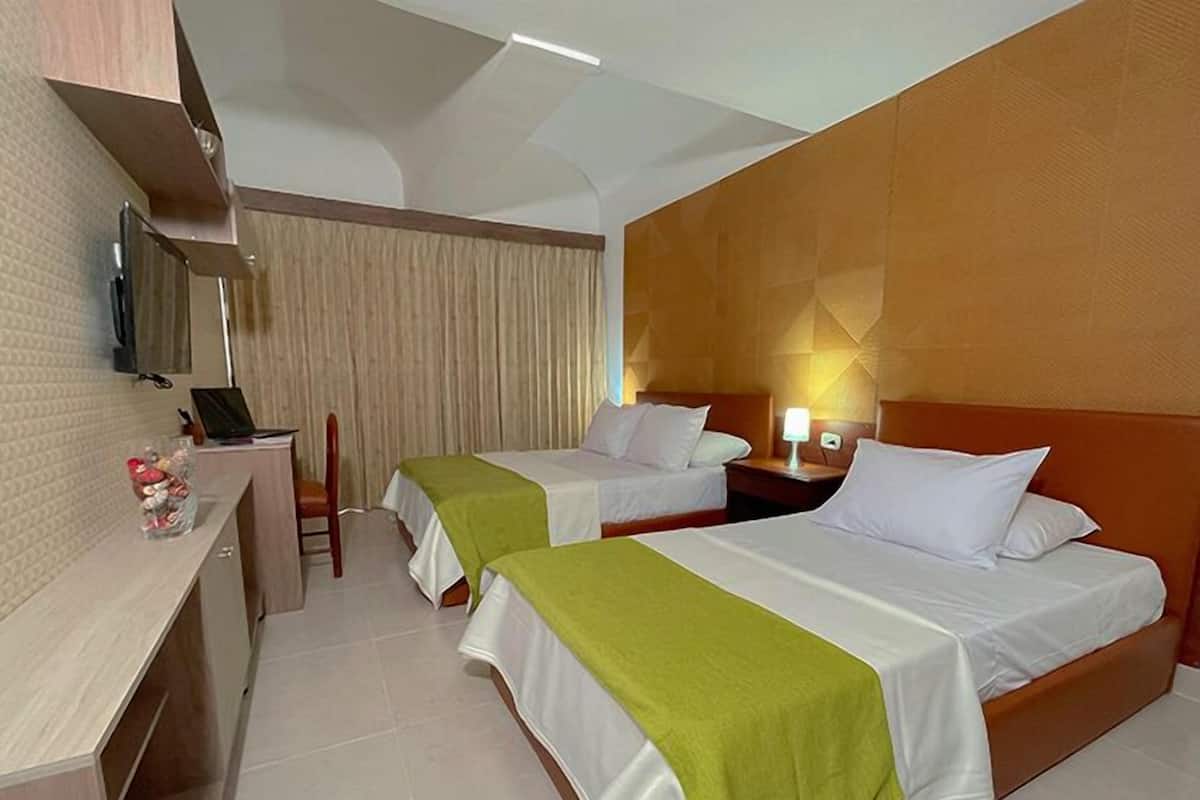 A hotel room with two beds, a desk, a chair, a lamp, and a mirror.