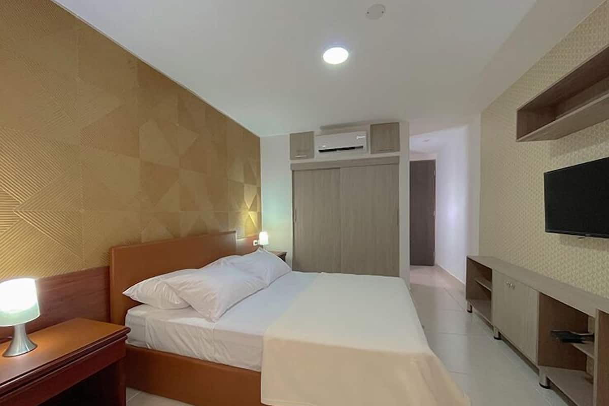 A hotel room with a bed, bedside lamp, wardrobe, and a TV mounted on the wall.