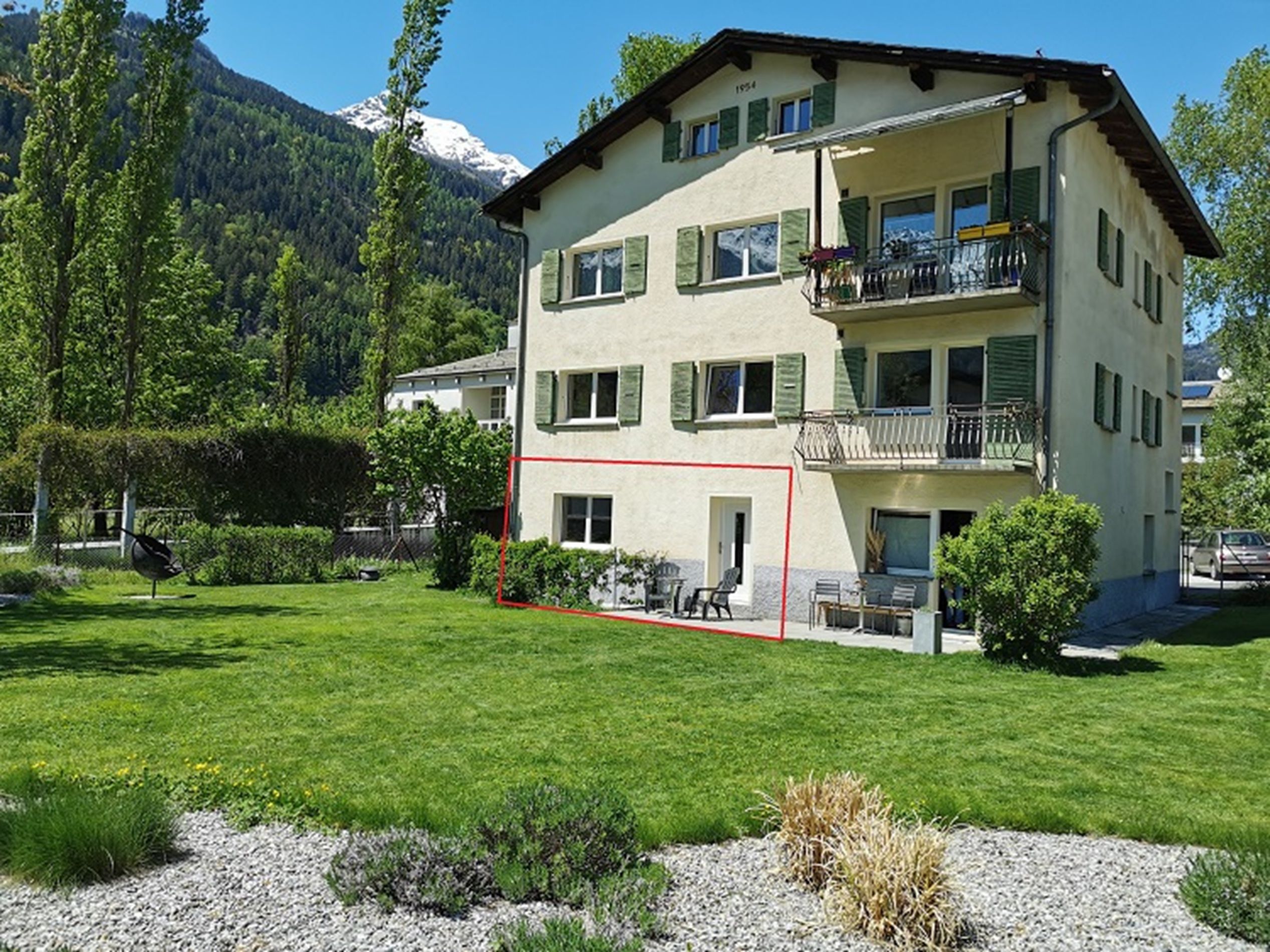 Un immeuble à plusieurs étages doté d’un balcon, entouré d’une pelouse bien entretenue et avec une chaîne de montagnes en toile de fond.